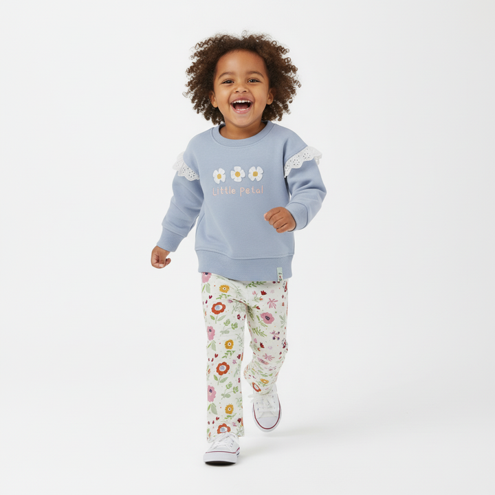 Child wearing a light blue sweatshirt with floral designs and white pants with colorful patterns on a white background