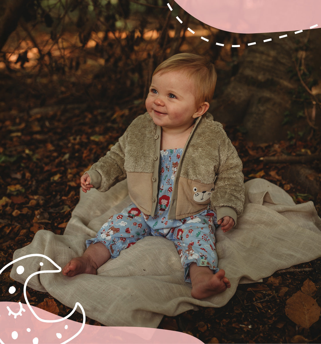 Baby sitting in a forest wearing Lilly and Sid printed romper and a beige borg fleece jacket. 