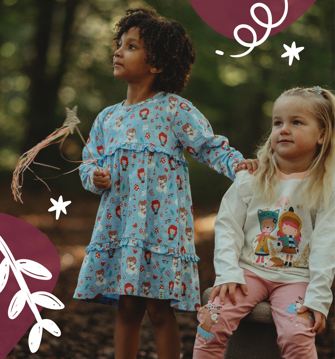 2 girls in a forest, one wearing wearing Lilly and Sid ruffle printed dress in blue and the other our pink and white matching natural set. 