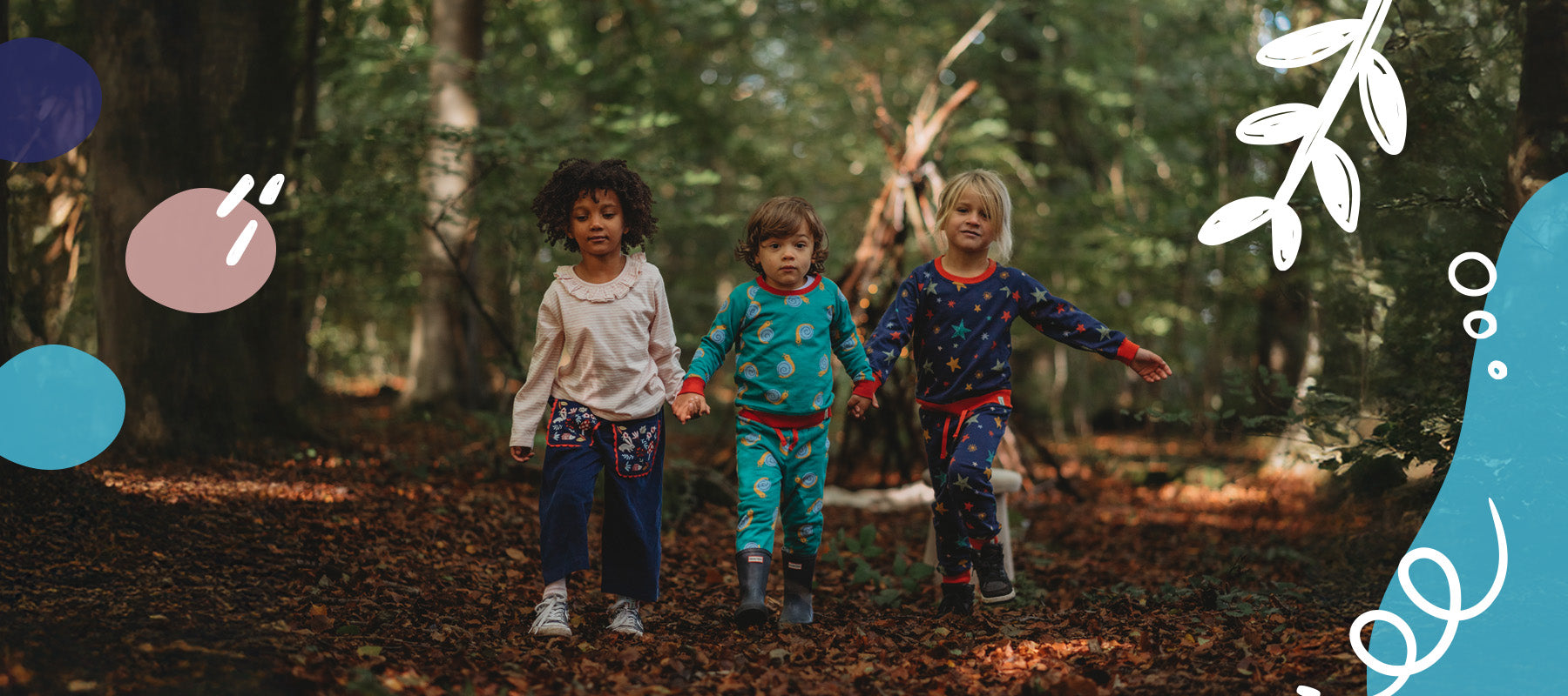 3 Children holding hands in a forest wearing printed Lilly and Sid organic matching sets. 