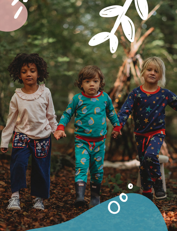 3 Children holding hands in a forest wearing printed Lilly and Sid organic matching sets.